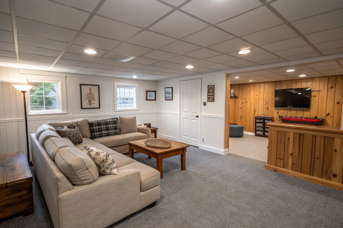 A dry finished basement rec room with a sectional sofa, painted paneling and a game table